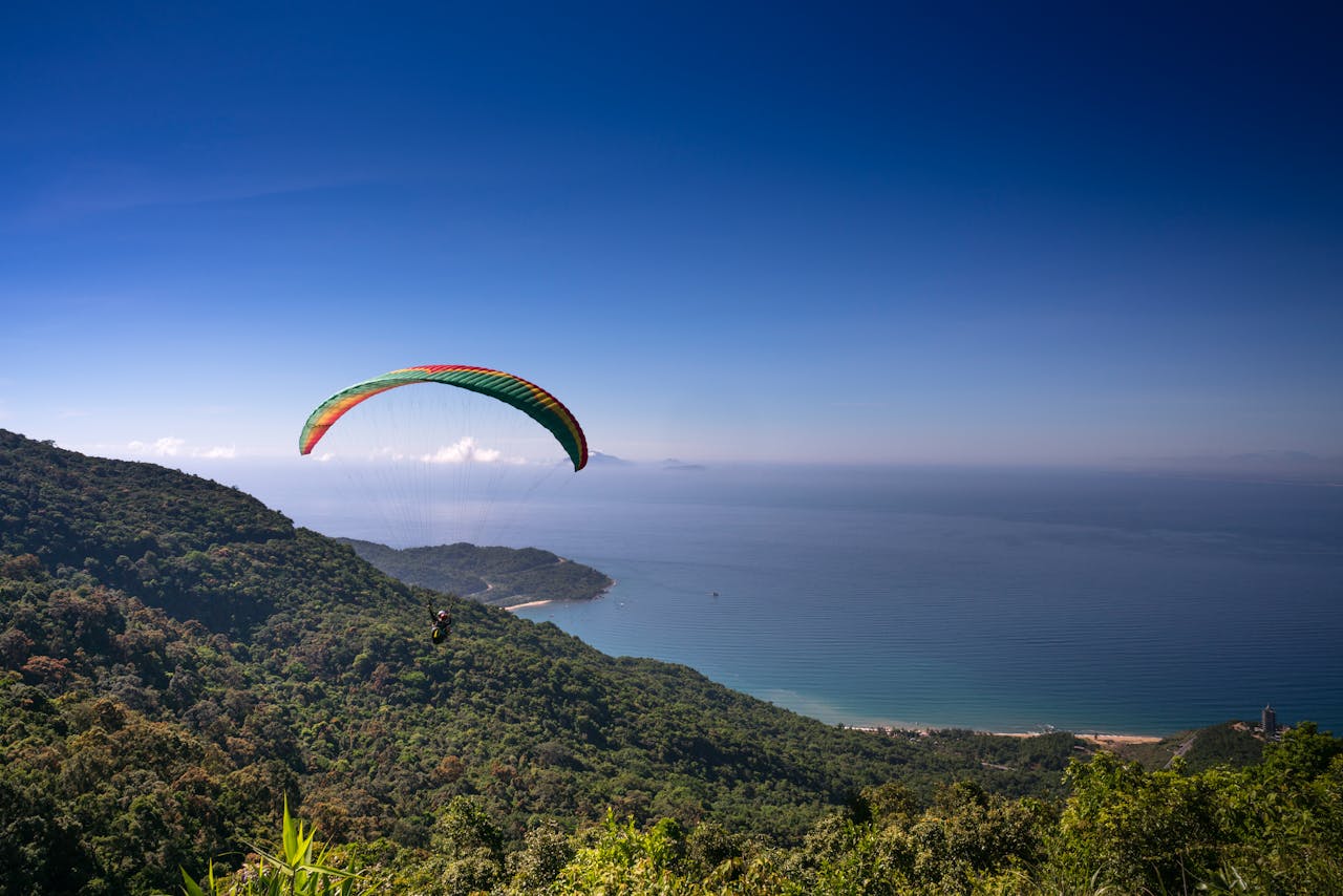 A paraglider soars above the lush Sơn Trà Peninsula with stunning ocean views in Đà Nẵng, Vietnam.