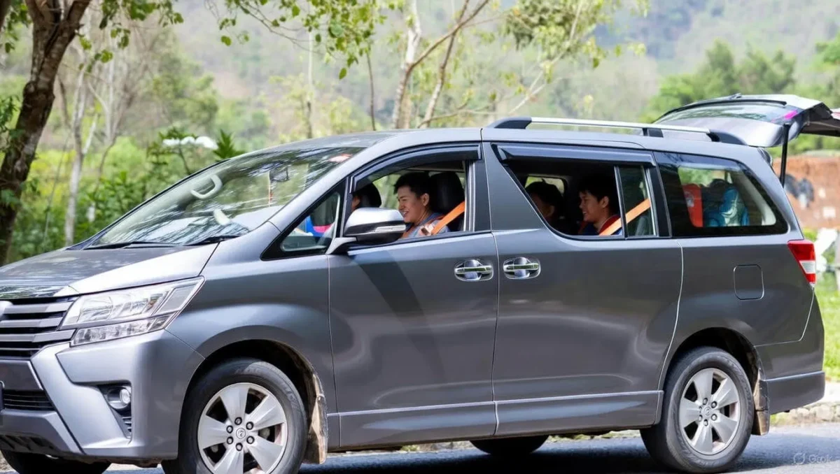 A side view of a grey 7-seater MPV with passengers inside and a trunk full of luggage parked in a forested area.