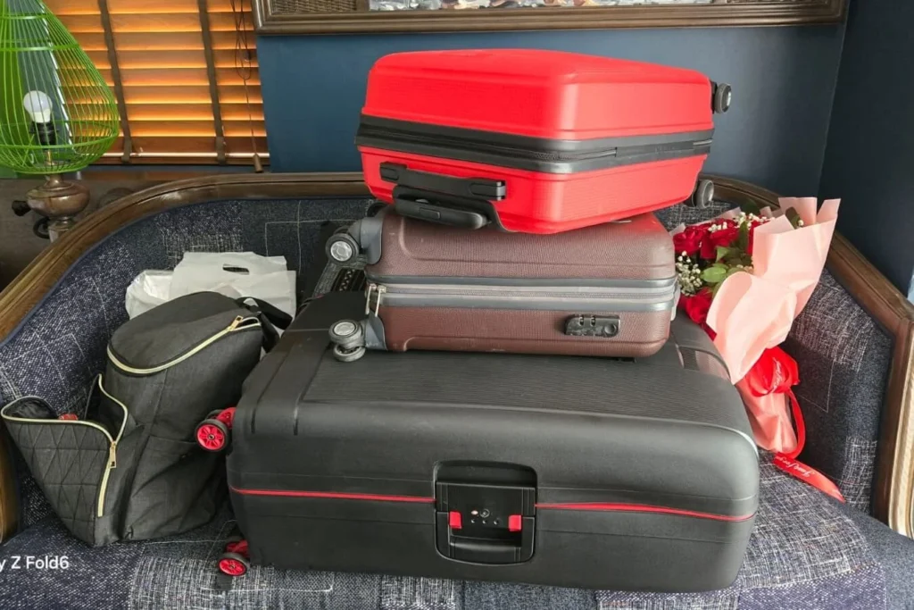 A stack of three large suitcases and two travel bags being organized for a trip.