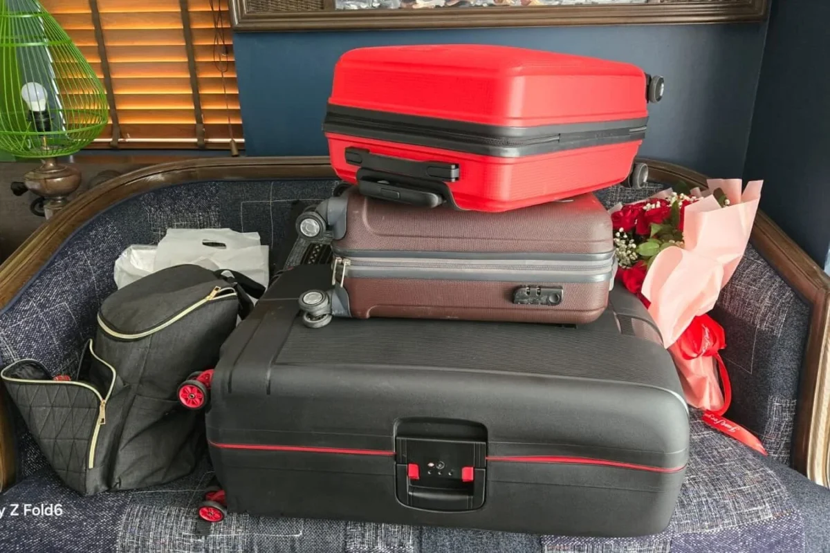 A stack of three large suitcases and two travel bags being organized for a trip.