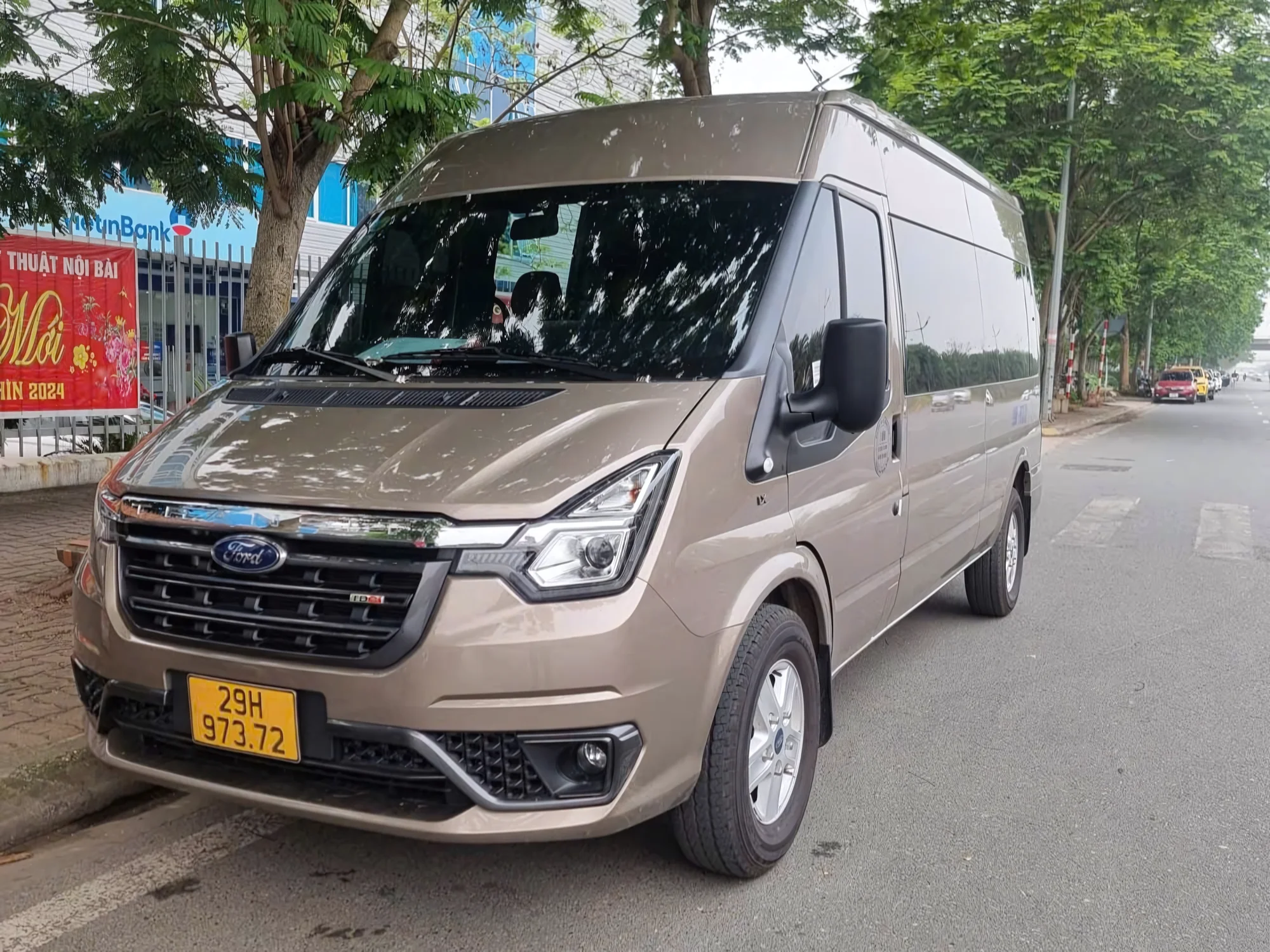 Beige 16-seat private van on a Vietnamese street — current-model exterior