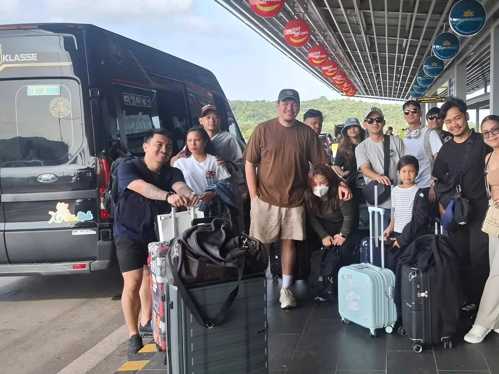 Group of travellers with luggage beside a 16-seat Private Vietnam van at an airport