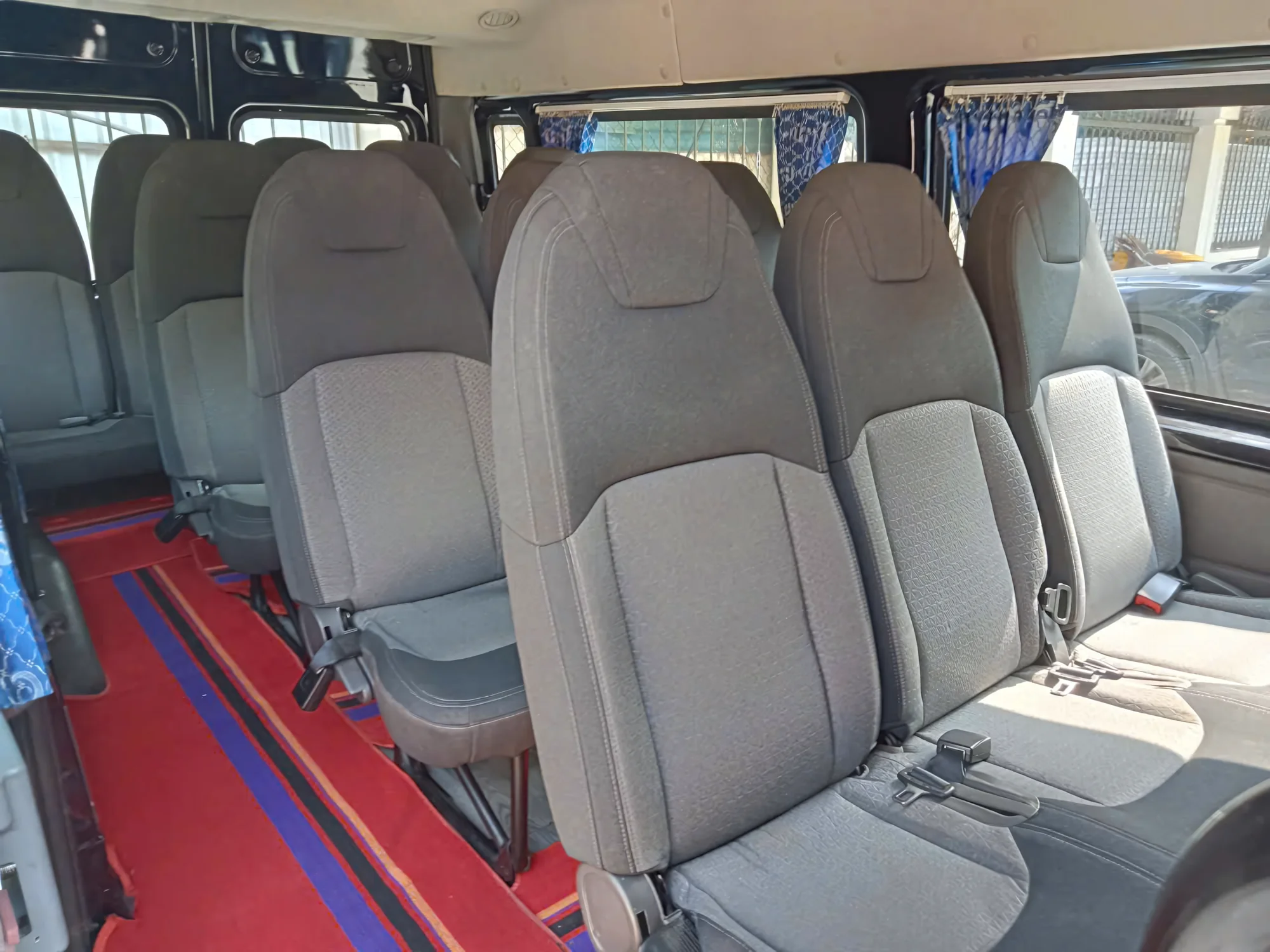 Rows of clean grey passenger seats inside a 16-seat private van