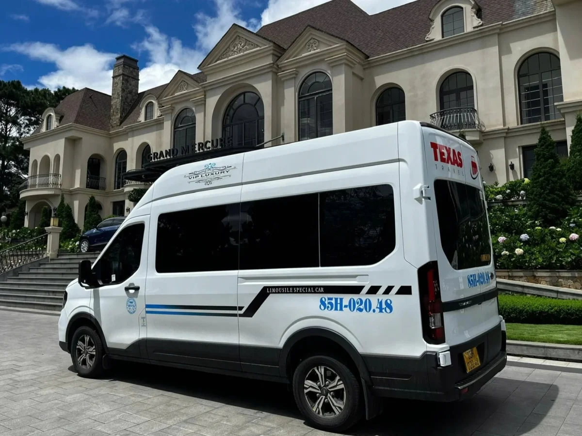 White 9-seat VIP van at a hotel entrance — luxury pickup for Hanoi to Ha Long Bay