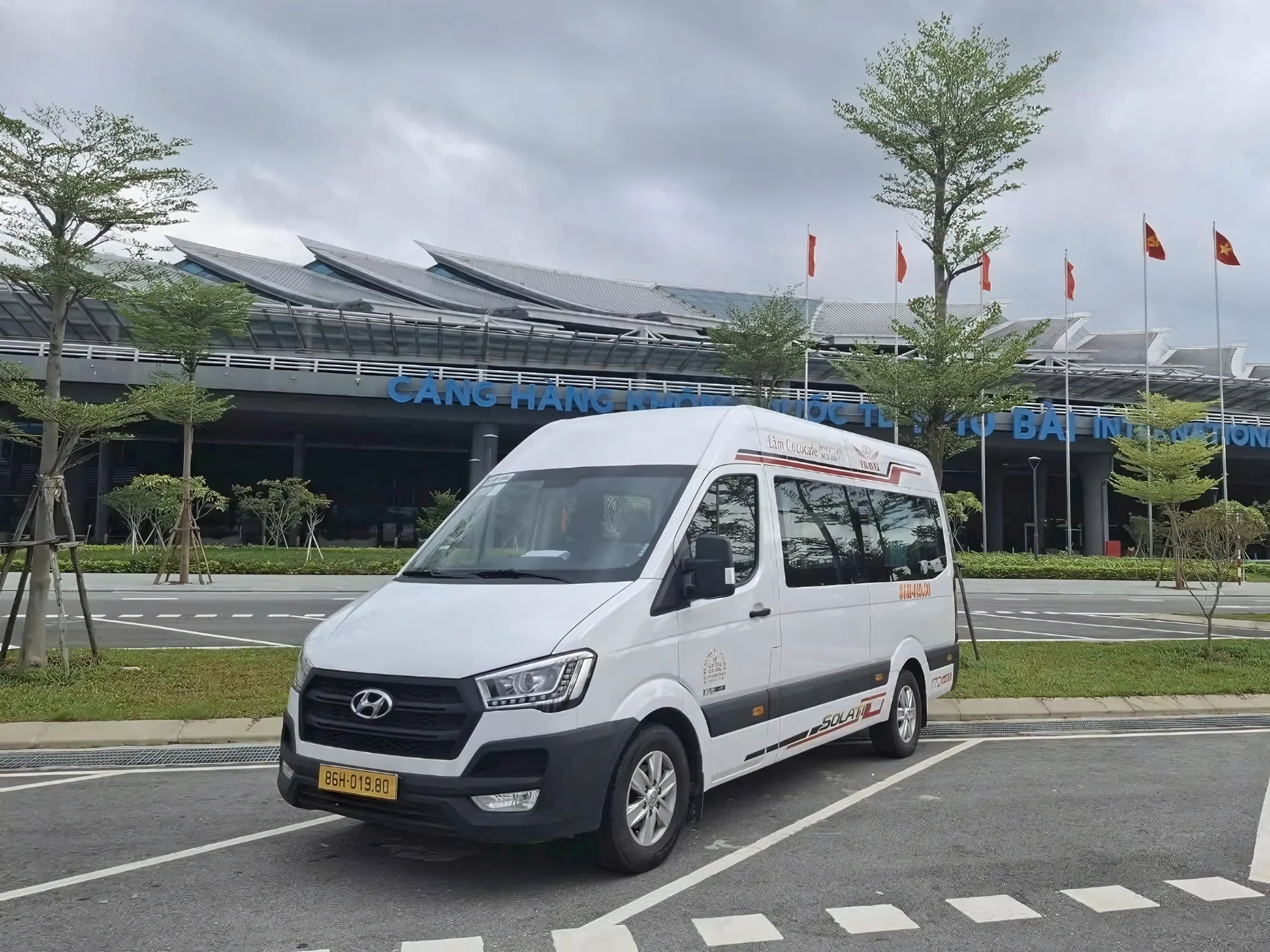White VIP van at a Vietnamese airport arrivals area with luggage