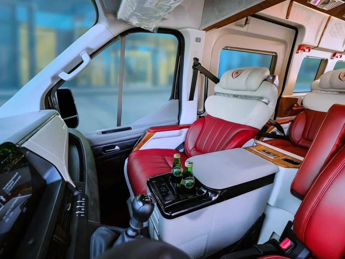 Interior of a premium VIP Dcar limousine van with red and white leather seating, a private chauffeur cockpit, and bottled water, used for private driver vietnam long distance transfers.