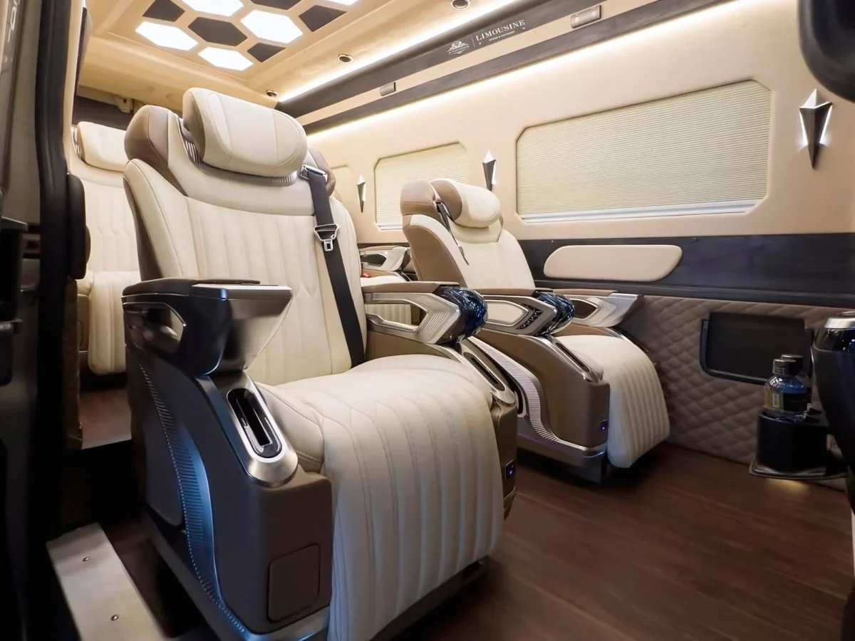 Close-up of reclining cream leather captain seats with armrest controls inside a premium van, showcasing a high-end vietnam private transfer and vietnam car rental with driver service.