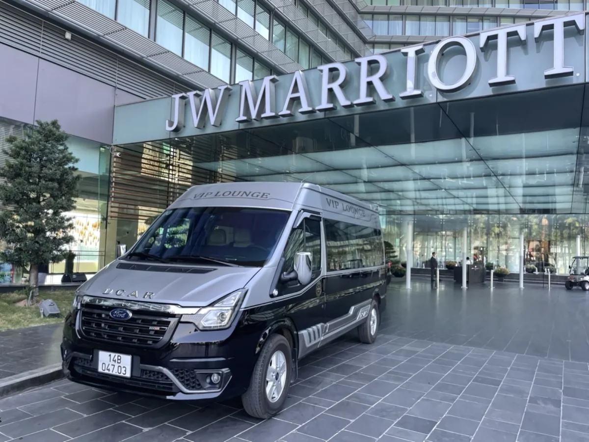 A two-tone premium Ford Transit DCar limousine van parked at a luxury hotel entrance for a seamless private transfer vietnam and private car hire vietnam service.